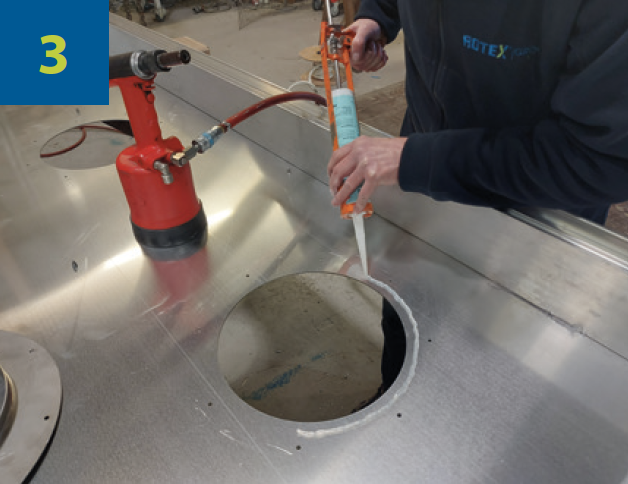 Industrial worker removing the ring and applying a bead of silicone RTV around the hole in the cover to seal the new inspection ring.